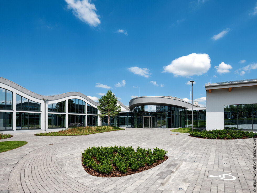 Bürogebäude in Paderborn mit geschwungenen Dächern und großen Fensterfronten, davor einen asphaltierten Platz mit bepflanzten Beeten